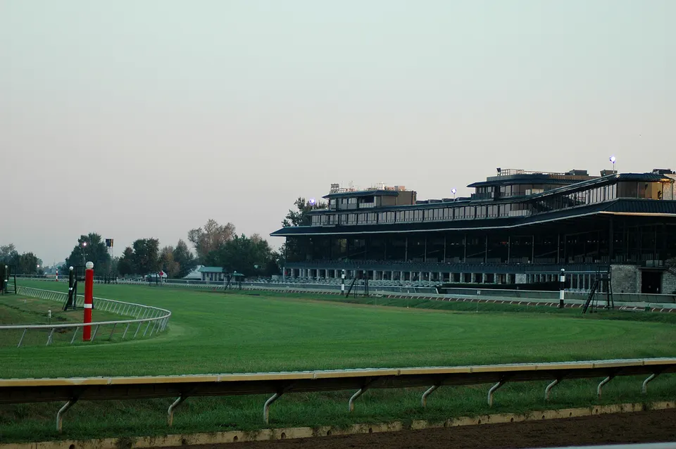 The empty grass and dirt track at Keeneland Race Course under a hazy early-morning sky, with the grandstand and red-and-white furlong poles in view, September 2005.